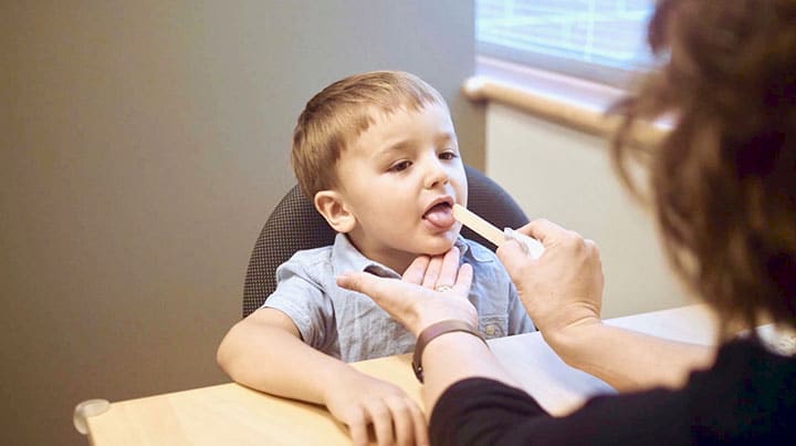 A child having their throat examined with a tongue depressor