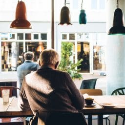 Older man sitting down inside a coffee shop.