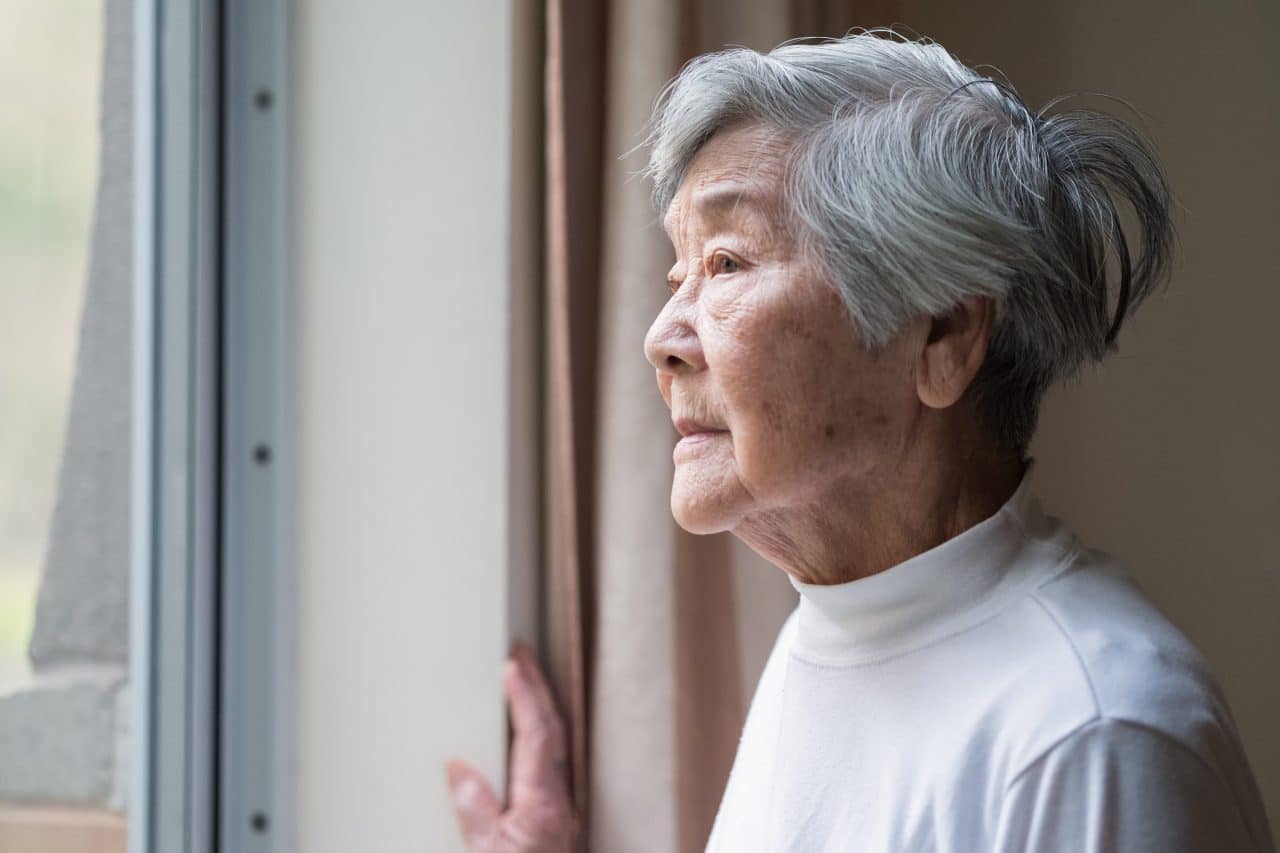 Older woman looking outside her window.