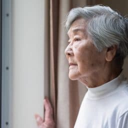 Older woman looking outside her window.