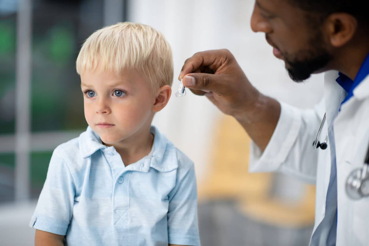 Audiologist fits a young boy with pediatric hearing aids.