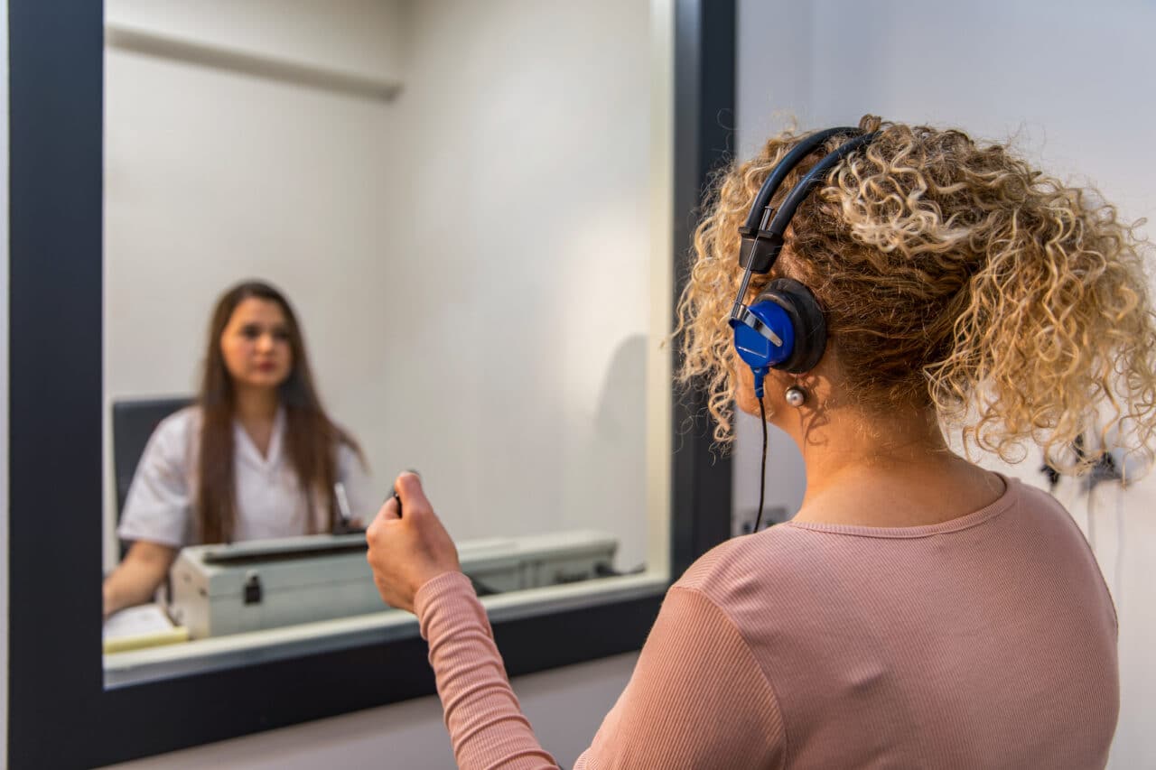 Woman gets a hearing test inside of an audiologist's sound booth.