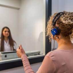 Woman gets a hearing test inside of an audiologist's sound booth.