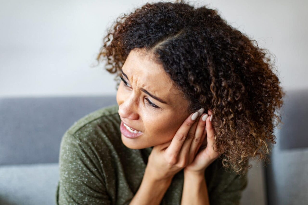 A woman experiencing ear pain holds her hand to her ear.