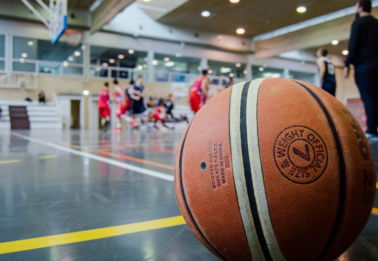 Close-up of a basketball with people playing in a gym in the background.