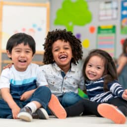 Three preschool-aged children sit in their classroom