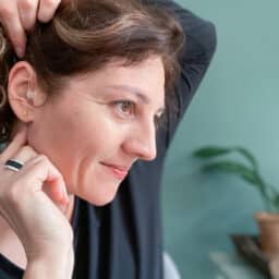 Woman touches hearing aid behind her ear