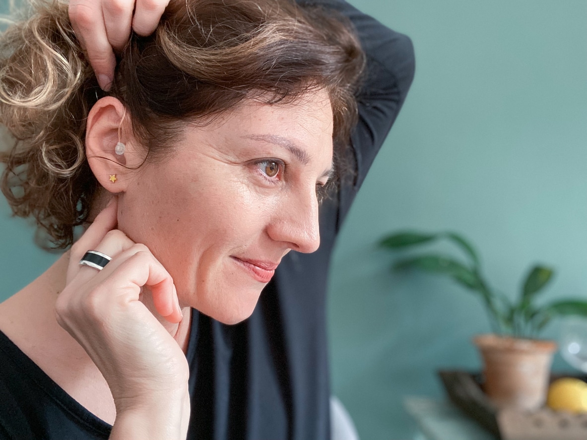 Woman touches hearing aid behind her ear