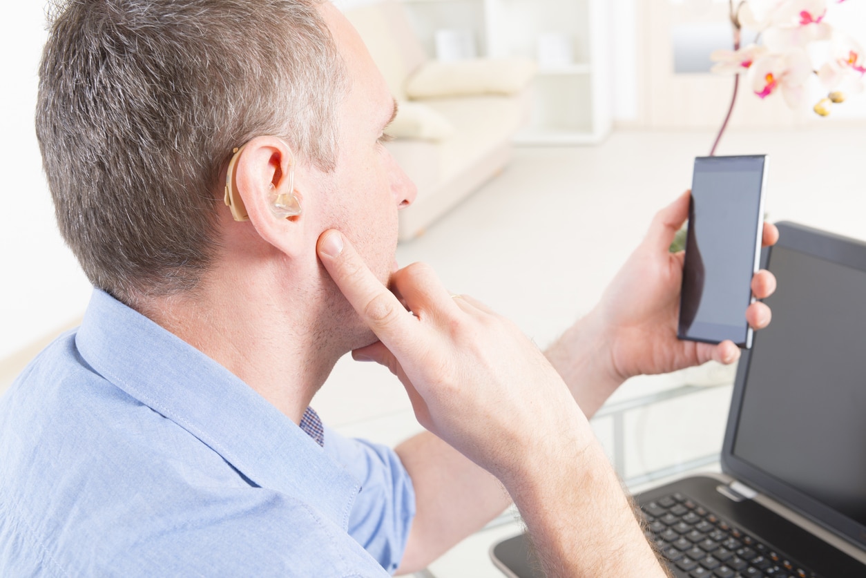 Man holding up a phone programming his hearing aids.