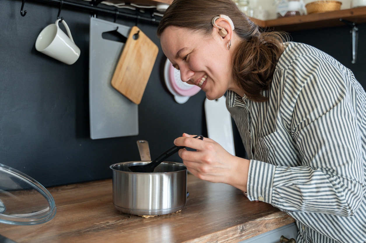 Woman with a hearing aid stirring a pot in the kitchen.