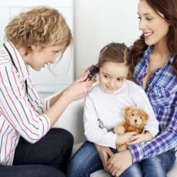 Young girl sitting in her mother's lap having her ear examined.