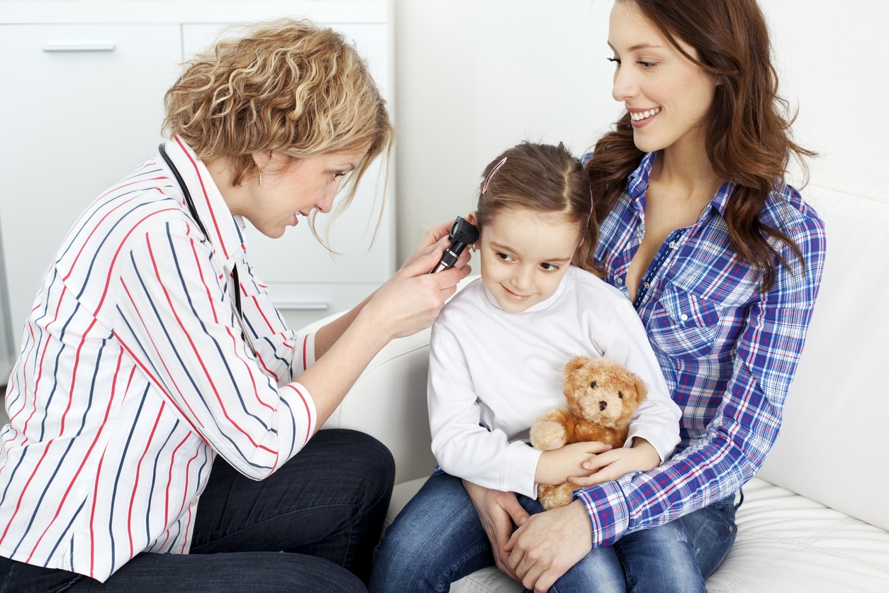 Young girl sitting in her mother's lap having her ear examined. 